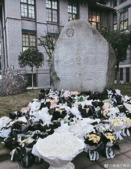The ground in front of a massive stele is a sea of flowers, crowded with funereal bouquets.